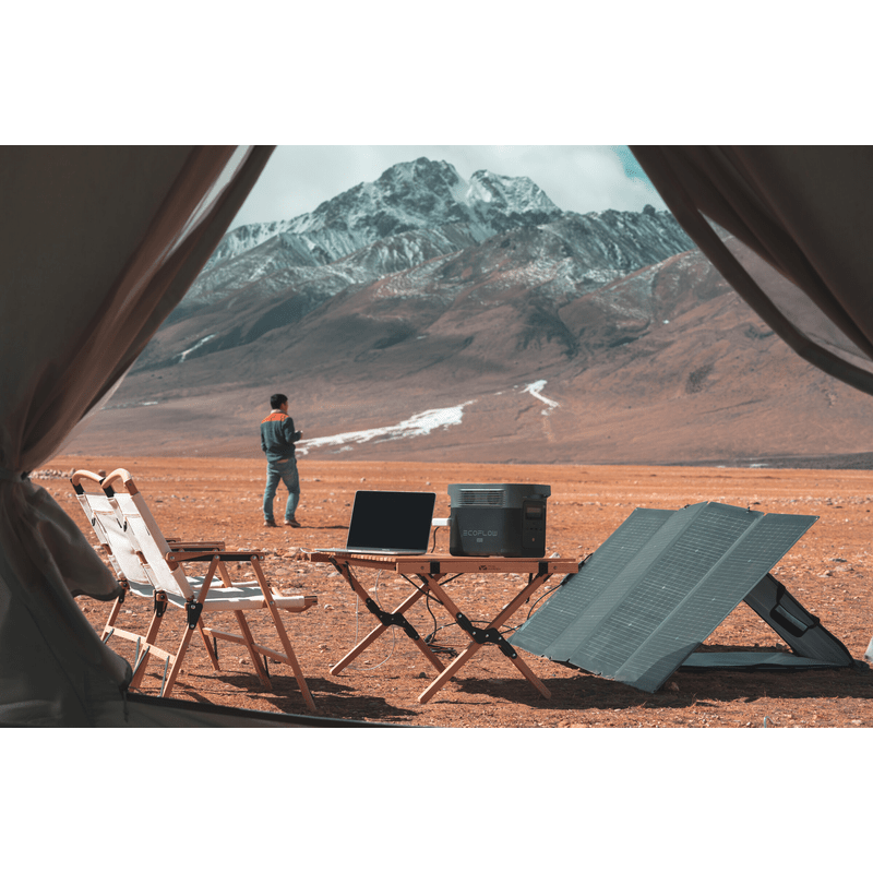 best foldable solar panel on display with man camping in mountain. Panel has kickstand and generator powering computer outside of tent. EcoFlow